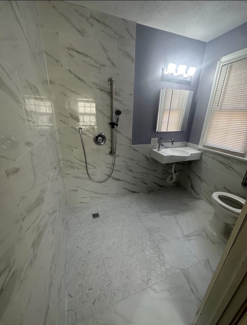 Accessible curbless walk-in shower with marble-look tile, grab bar and wall-mounted sink